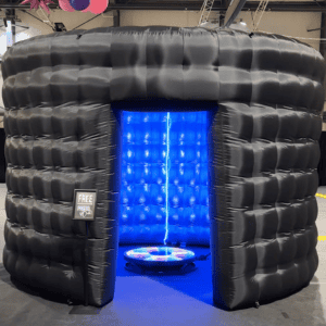 Black inflatable photo booth with blue LED interior lighting at an event.